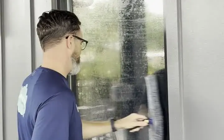 Nick Mattia, owner of Shine Above, washing a window with a scrubber and squeegee